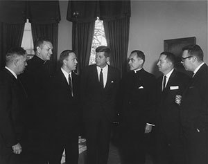 President John F. Kennedy is presented the 1961 Laetare Medal in the Oval Office. Attending the presentation (L-R): unidentified man; Father Edmund P. Joyce, C.S.C., vice president of Notre Dame; Rep. John Brademas, Indiana; Kennedy; Rev. Theodore M. Hesburgh, C.S.C., president of Notre Dame; James E. Murphy, director of public relations at Notre Dame; and an unidentified man.