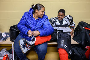 Lateese Williams helps her son Jon, 10, put on his new hockey gear in a Compton Family Ice Center locker room. Photo by Matt Cashore/University of Notre Dame.