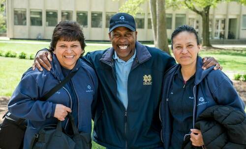Three Building Services staff members pose smiling outside of a campus building