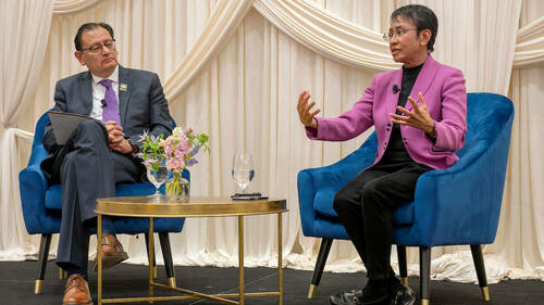 Andrés Mejía Acosta and Maria Ressa sit on blue velvet chairs on a stage with white drapes in the background, answering audience questions