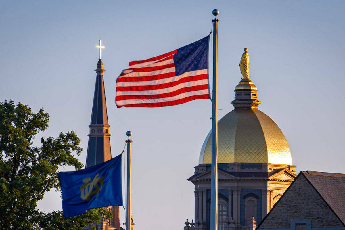 The Notre Dame and U.S. flags fly in front of the campus skyline (Photo by Matt Cashore/University of Notre Dame)