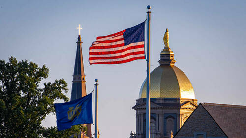 The Notre Dame and U.S. flags fly in front of the campus skyline (Photo by Matt Cashore/University of Notre Dame)