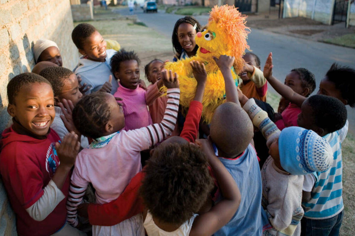 South African children play with Kami, a furry yellow five-year-old HIV-positive girl muppet orphaned by AIDS. ©2007 Sesame Workshop. All Rights Reserved. Photographed by Ryan Heffernan.