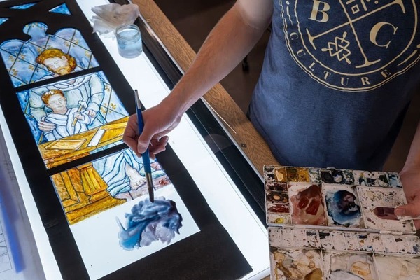 A students paints a luminaire — a mockup of the window painted onto clear acetate and framed, so that light can shine through it