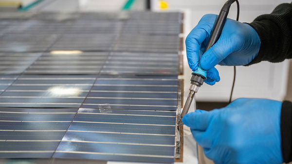 A close-up of a person in blue, synthetic rubber gloves soldering a solar cell.