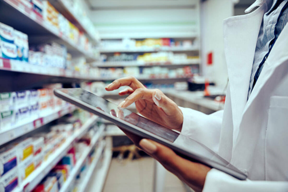 Pharmacist holds tablet in front of an aisle of medicines.