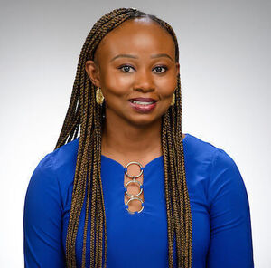 Female professor with long dark braids wearing a bright blue blouse and gold earrings.