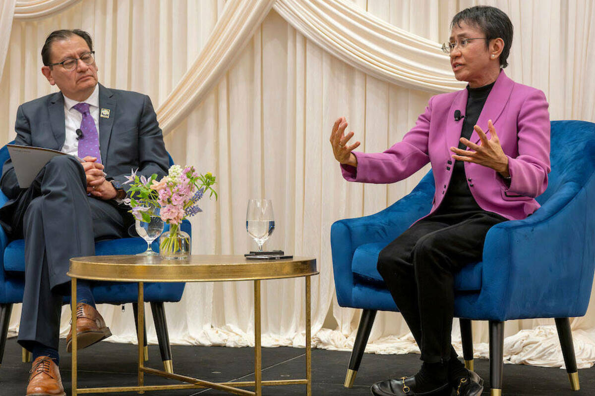 Andrés Mejía Acosta and Maria Ressa sit on blue velvet chairs on a stage with white drapes in the background, answering audience questions