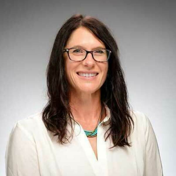 Tracy Kijewski-Correa, female professor is pictured seated, smiling, in front of a gray backdrop. She has long dark hair and glasses.