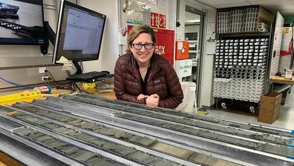 Melissa Burke stands with multiple rows of core samples aboard the JOIDES Resolution research vessel.