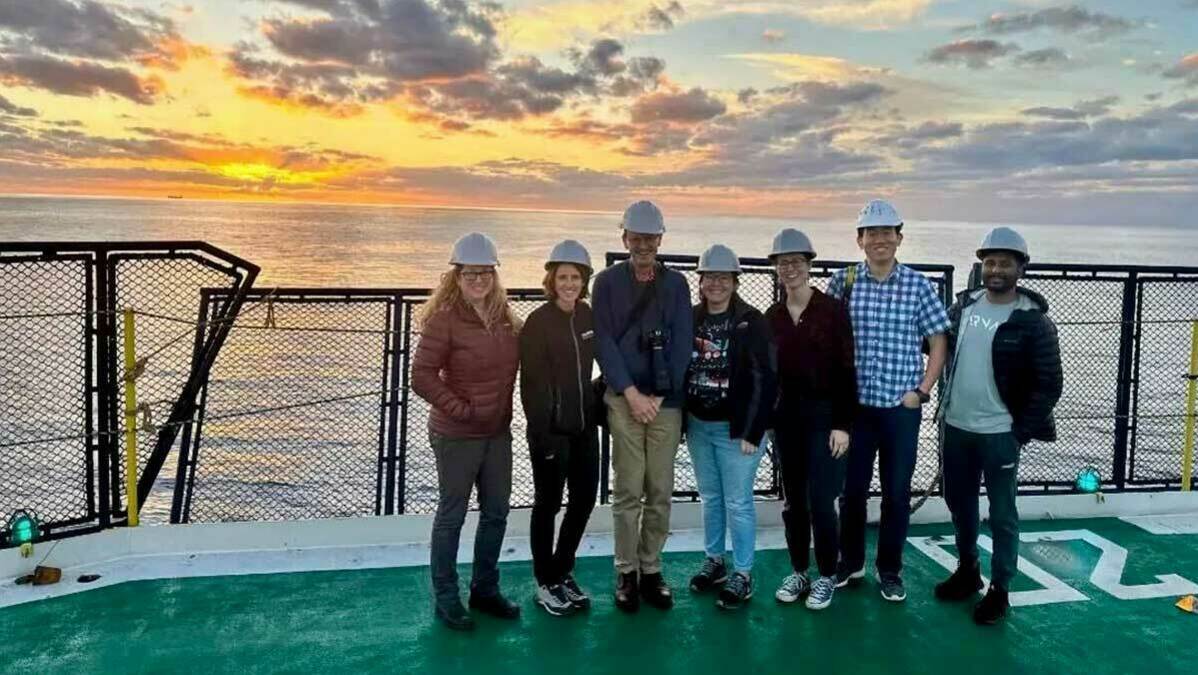 Melissa Berke aboard the JOIDES research vessel with other scientists. A sunset is in the background.