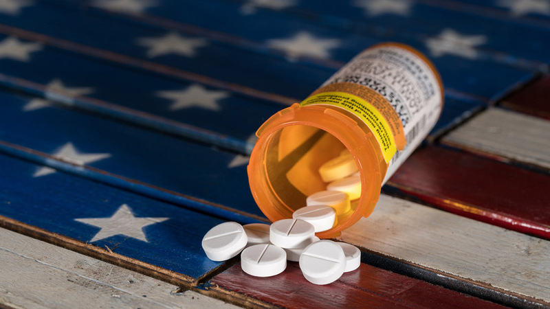 Photo of spilled bottle of prescription pills onto a wooden table that is designed to look like the U.S. Flag.
