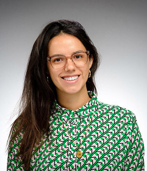 Vicky Barone is pictured wearing a bright green checkered blouse and has long dark hair and glasses.