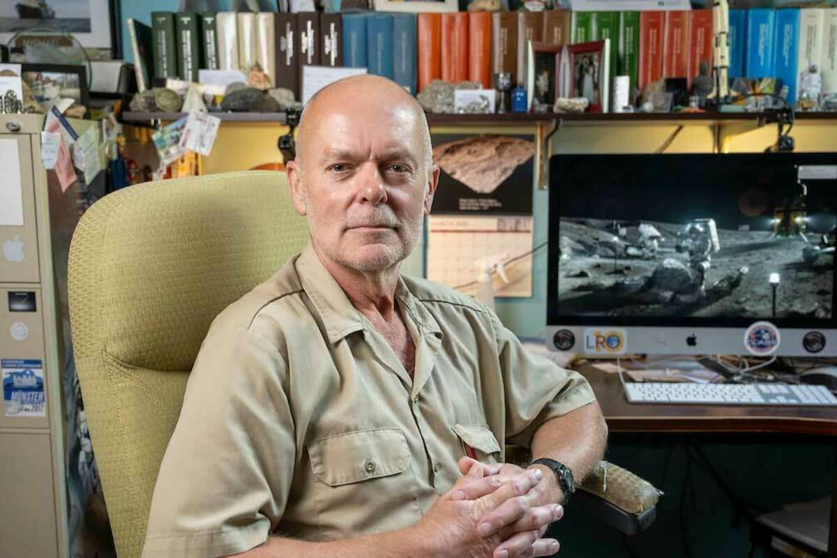 Clive Neal sits in his office, framed by a filing cabinet, and shelves of scientific journals. An image of the 1969 Moon landing is on a computer screen behind him.