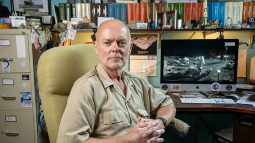 Clive Neal sits in his office, framed by a filing cabinet, and shelves of scientific journals. An image of the 1969 Moon landing is on a computer screen behind him.