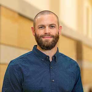 Richard Marcantonio smiles standing in a hallway on the University of Notre Dame campus. He is wearing a blue button up shirt and has a short beard.