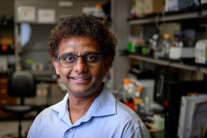 Man with brown curly hair and brown skin in light blue button-down shirt in a lab.