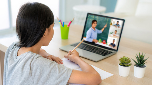 Young middle school student with long black hair sits at her desk in front of a laptop where you can see on the screen that a teacher is giving virtual instruction.