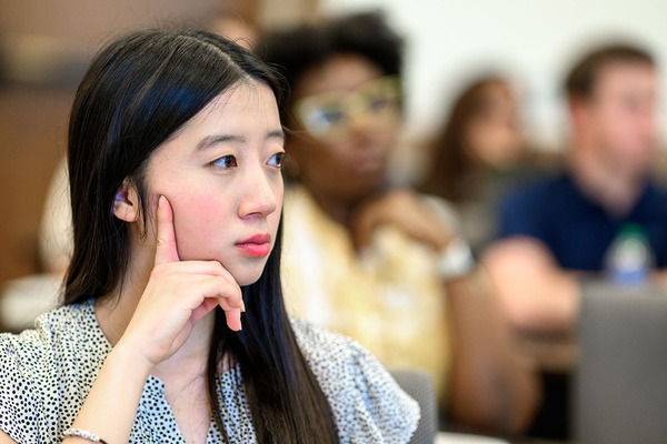 Female student with long black hair listens to a lecture in a classroom.